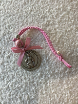 A silver medallion featuring Jesus Christ with a pink miniature Mati charm on top, attached to a pink cord with a rose-colored bead