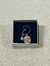 A silver pin with an oval pendant featuring an image of the Panagia holding baby Jesus, accompanied by a small Mati charm, presented in a gift box.