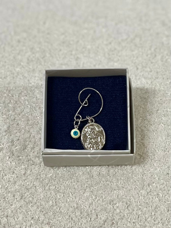 A silver pin with an oval pendant featuring an image of the Panagia holding baby Jesus, accompanied by a small Mati charm, presented in a gift box.